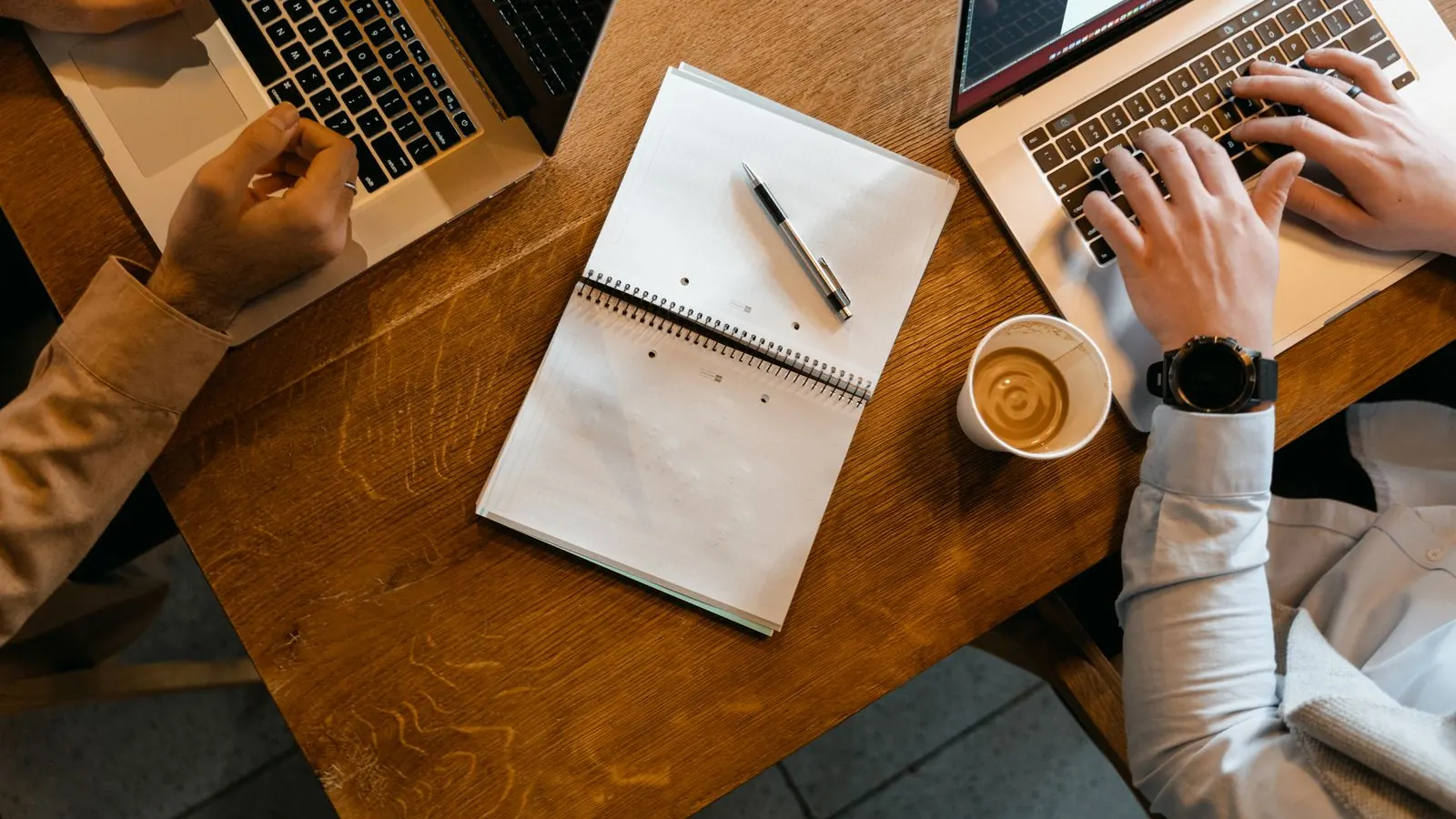 Overhead view of a small team working on laptops with a notebook and coffee