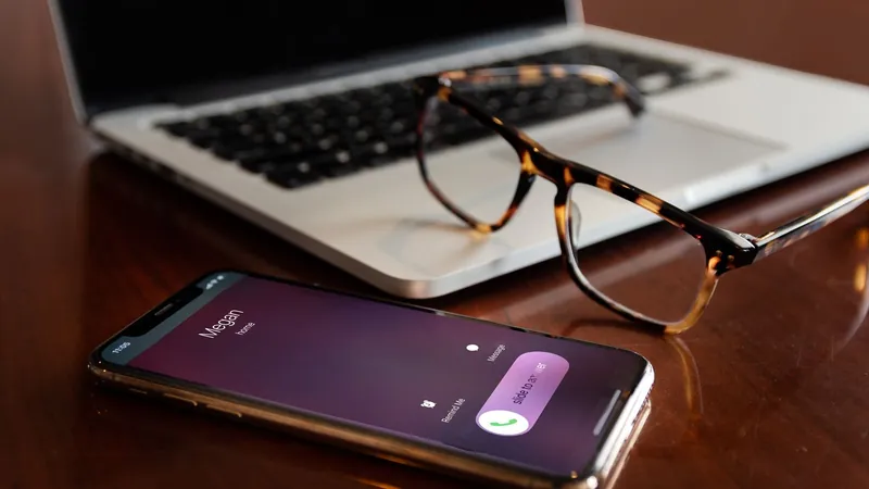 Smartphone showing an incoming call next to a laptop on a desk